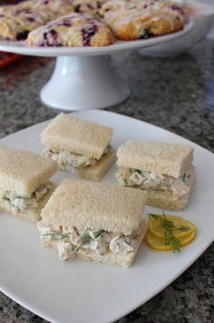 four sandwiches on a white plate with lemon wedges next to it and a cake in the background