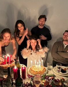 a group of people standing around a table with cake and candles in front of them