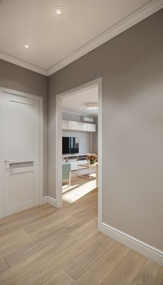 an empty living room with wood flooring and white doors leading to the kitchen area