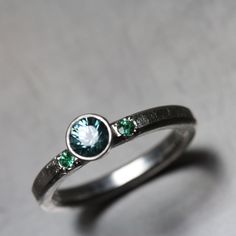 Gorgeous blue green ocean hues. A perfect engagement ring for a caribbean wedding! The center stone is a beautiful 4.5mm blue zircon. On each side I bead set one 2mm emerald. A dreamy color combination for your bride to be. I fabricated a ring from sterling silver wire and tubing and set gemstones worthy of a mermaid (Meerjungfrau) in it. A gently hammered texture and a diamond finish adds extra sparkle. Shank measures 2.5mm in width and 2mm in thickness. Shown in size 5 or 49.5 or small 16 (in Green Sapphire Jewelry With Halo Setting, Green Aquamarine Rings For Anniversary, Green Aquamarine Promise Ring, Green Sapphire Sterling Silver Ring For Wedding, Aquamarine Rings With Bezel Setting For Wedding, Bezel Set Aquamarine Wedding Rings, Wedding Rings With Aquamarine And Bezel Setting, Green Sapphire Wedding Ring Birthstone, Green Jewelry With Bezel Setting For Wedding