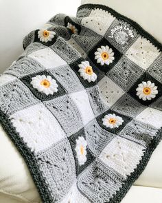 a crocheted blanket with flowers on it sitting on a white couch next to a pillow