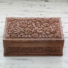 an intricately carved wooden box sitting on top of a white wood table with flowers and leaves