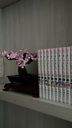 the books are lined up on the shelf next to the vase with flowers in it