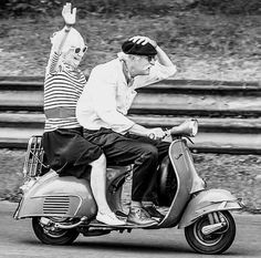 two people riding on the back of a scooter with their arms in the air