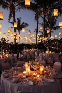 an outdoor dinner setting with paper lanterns in the sky and candles lit on the tables