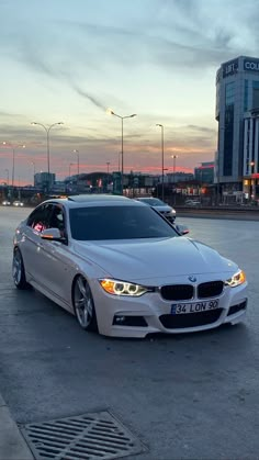 a white car is parked in an empty parking lot at dusk with the sun setting behind it