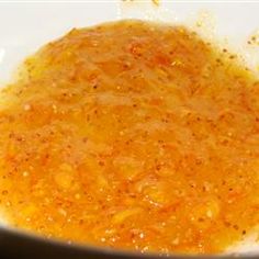 a white bowl filled with orange sauce on top of a wooden table next to a knife and fork