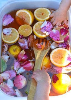 a person holding a wooden spoon in a tub full of water with lemons and rose petals