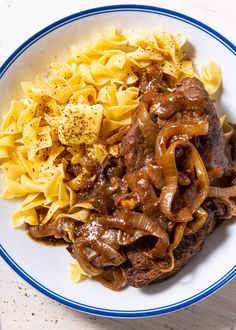 a white plate topped with pasta and meat covered in gravy on top of a wooden table