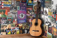 an acoustic guitar sitting on top of a wooden floor next to a wall covered in posters