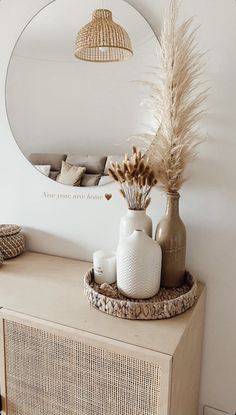 a vase with dried flowers on top of a dresser next to a round mirror and wicker basket