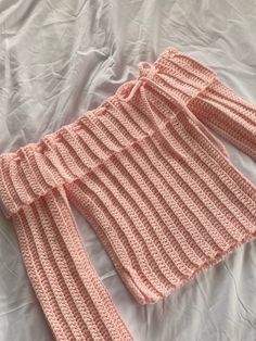 a pink knitted sweater laying on top of a bed