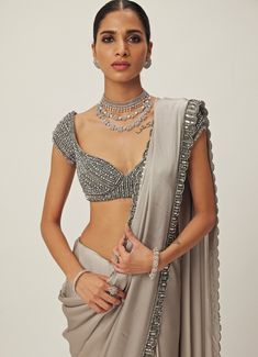 This exquisite Grey Crystal and Sequin Hand Embroidered Satin Saree Set is the perfect fusion of traditional elegance and modern sophistication. Made from luxurious satin and georgette, the grey saree features intricate hand embroidery with shimmering sequins and tonal crystal embellishments along the borders, offering a subtle yet opulent look. Paired with a cap-sleeved blouse adorned with sparkling crystal accents, jewelled design that adds a chic, contemporary twist. Ideal for Mehndi, Sangeet ceremonies, or as a statement saree at reception. Composition : Saree - Satin and Blouse - Georgette Care: Dry Clean Only and Vacuum Storage This product can be customized for sleeves, blouse length and neckline Delivery : 6-8 weeks as the product is hand crafted. Check Size Guide or choose MySize Grey Satin Saree, Satin Saree Blouse, Satin Sari, Saree Satin, Sequin Saree, Grey Saree, Crystal Embroidery, Vacuum Storage, Cap Sleeves Blouse