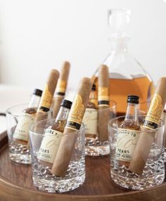 several bottles and glasses with cigars in them on a wooden tray next to a bottle of liquor