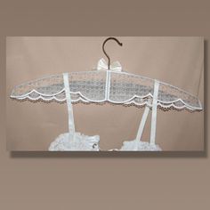 an umbrella with white lace on it hanging from a hanger in front of a beige wall