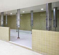 an empty bathroom with green tiled walls and mirrors on the wall, in front of a row of urinals