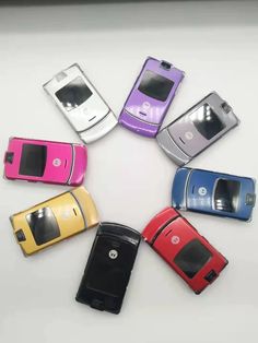 six cell phones arranged in a circle on top of a white table with one open and the other closed