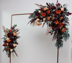 two tall floral arrangements with orange and red flowers are on display in front of a white wall