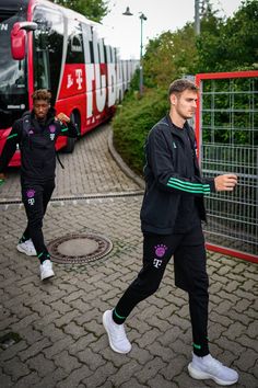 two men in black tracksuits are walking near a bus