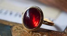 The Classic Dragon Breath Vintage Ring features a mesmerizing deep red garnet stone that captures the light with every turn. Set in a classic gold band with delicate beaded detailing, this ring exudes a timeless elegance. The rich crimson hue of the garnet adds a bold pop of color, making it a striking accessory for any occasion. Perfect for those who appreciate vintage-inspired pieces with a modern twist, the Classic Halo Vintage Ring is designed to enhance your look with a touch of sophistication and charm. Details Classic Halo Vintage Ring in Red Gold pleated Adjustable opening Missy Jewelry Dragon Breath Collection Classic Red Ruby Ring, Oval Cabochon, Elegant Gold Garnet Cabochon Jewelry, Classic Red Ruby Ring With Oval Cabochon, Classic Red Ruby Jewelry, Classic Red Ring With Bezel Setting, Classic Red Rings With Bezel Setting, Classic Red Bezel Set Ring, Elegant Round Cabochon Ruby Ring, Elegant Red Cabochon Jewelry