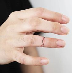 a woman's hand with a small ring on her left thumb and a red line tattoo on the middle finger