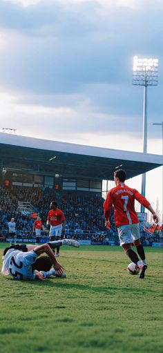 two men playing soccer on a field with fans in the stands watching from the stands