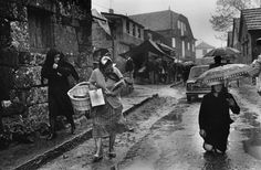 an old black and white photo of people walking in the rain