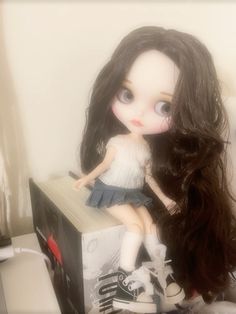 a doll sitting on top of a box with long black hair in it's hands