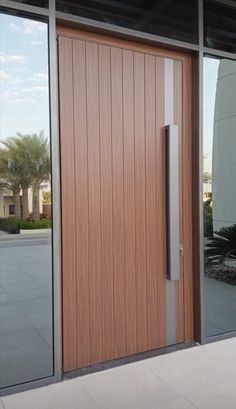 a large wooden door sitting inside of a glass window next to a sidewalk and palm trees