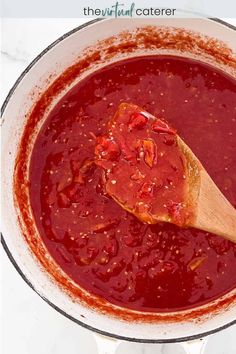 a wooden spoon in a pot filled with red sauce