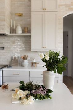 two white vases with flowers on a kitchen counter