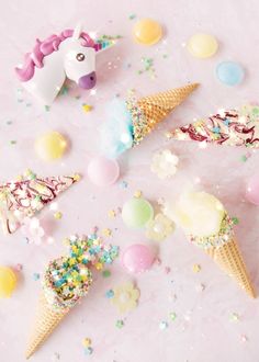 three ice cream cones with sprinkles and candies around them on a white surface