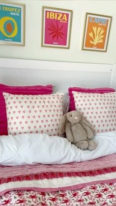 a teddy bear sitting on top of a bed next to two framed pictures above it