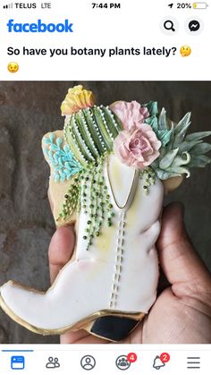 a hand holding a cookie shaped like a cowboy boot with flowers on the top and side