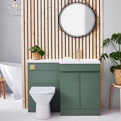 a white toilet sitting next to a green cabinet in a bathroom under a round mirror