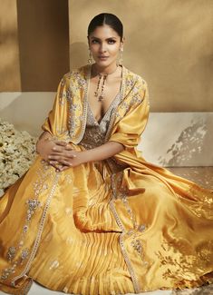 Editor's Note Indulge in vivacious elegance with this Haldi Yellow Venetian Cape Set. Crafted from silk Chanderi, it showcases luxe hand embroidery in Resham Ari, Zardozi, Sheesha, and sequins. The cape features delicate floral embroidery, while the lehenga skirt boasts handloom woven Banarasi with gathers at the waist and an embellished belt. The blouse dazzles with an inverted-V deep neckline and Sheesha work. Fabric: Silk Color: Yellow Components: Cape, skirt and blouse Disclaimer: Product co Silk Traditional Wear With Cutdana Detailing For Reception, Silk Traditional Wear With Cutdana For Reception, Elegant Yellow Dola Silk Anarkali Set, Silk Sets For Navratri Reception, Silk Sets For Reception At Navratri Festival, Silk Sets For Reception And Navratri, Chanderi Kurta With Gold Embroidery For Reception, Floor-length Silk Kurta For Reception, Elegant Yellow Silk Sharara