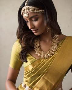 a woman in a yellow sari and gold jewelry is looking down at her wrist