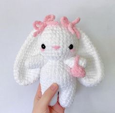 a hand holding a small white crocheted stuffed animal with pink bows on it's head