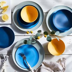 four plates with blue and yellow painted on them next to utensils, lemon wedges and silverware