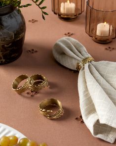 two napkins and some gold rings on a table with candles in the back ground