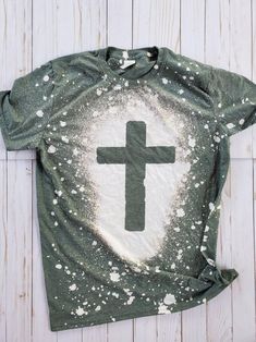 a t - shirt with a cross painted on the front and white splatters all over it