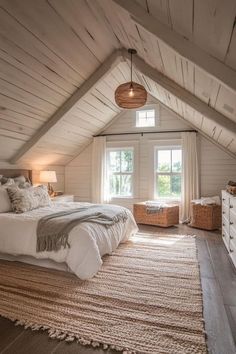 an attic bedroom with white walls and wood flooring is furnished with natural materials such as rugs, bedding, and pillows