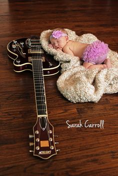 a baby laying on top of a blanket next to a guitar