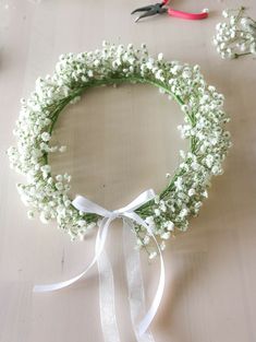 a wreath with white flowers tied around it and scissors on the table next to it