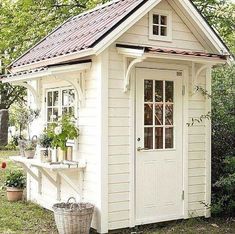 a small white shed sitting in the middle of a yard with potted plants on it