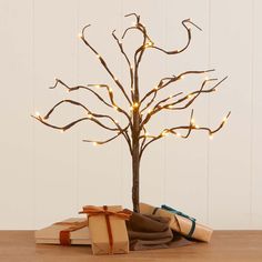 a small tree with lights on it sitting next to some books and wrapped presents in front of a white wall