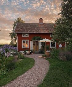 a red house with an umbrella in front of it on a gravel path leading to the door