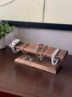 a wooden stand with bracelets and rings on it next to a potted plant