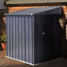 a small metal shed sitting in the middle of a yard with potted plants around it