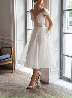 a woman standing in front of a window wearing a white dress